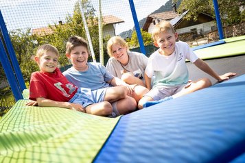 Vier Kinder sitzen fröhlich auf einem großen Trampolin im Familienhotel Krone im Allgäu.