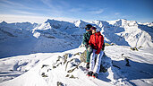 Winter im Salzburger Land: Paar sitzt auf dem Gipfel Sportgastein mit einer herrlichen Aussicht.