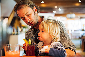 Vater sitzt mit seinem Kind an der Bar des Familienhotels Kirchheimerhof in Kärnten und genießt ein Kaltgetränk.
