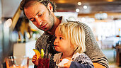 Vater sitzt mit seinem Kind an der Bar des Familienhotels Kirchheimerhof in Kärnten und genießt ein Kaltgetränk.