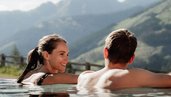 Ein Paar entspannt gemeinsam im Outdoor-Pool des Familienhotels Scherer mit Blick auf die Bergkulisse.
