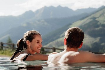 Ein Paar entspannt gemeinsam im Outdoor-Pool des Familienhotels Scherer mit Blick auf die Bergkulisse.