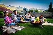 Eine Familie sitzt im Garten vom Adler Familien- & Wohlfühlhotel in Tirol und braten Marshmallows am Lagerfeuer.
