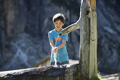 Jugendlicher Junge erfrischt sich am kalten Bergwasser beim Wandern im Familienurlaub in Tirol.