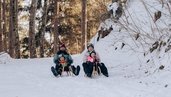 Familie fährt gemeinsam mit dem Schlitten durch die verschneite Winterlandschaft im Familienhotel Amiamo im Salzburger Land