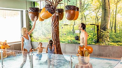 Eltern spielen mit ihren Kindern im Kinderschwimmbecken im Familienhotel Das Bayrischzell in Oberbayern.