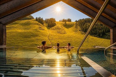 Mehrere Personen sitzen im Außenpool des Zauchenseehofs im Salzburger Land, während die Abendsonne über den Bergen scheint.
