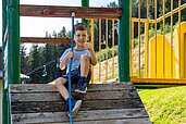 Ein Junge sitzt auf dem Außen-Spielplatz des Familienhotels Alpengasthof Hochegger auf einem Klettergerüst.
