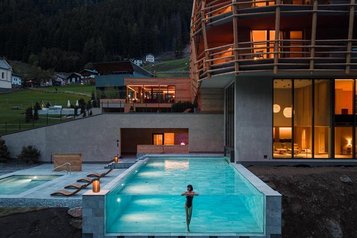 Neubau des Familienhotel Bella Vista in Südtirol bei Nacht mit beleuchtetem Infinity Pool und Blick zur Kirche.