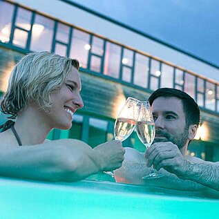 Eltern trinken im Pool des Familienhotels ein Glas Prosecco und geniessen die Aussicht im Outdoor-Pool