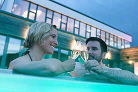Eltern trinken im Pool des Familienhotels ein Glas Prosecco und geniessen die Aussicht im Outdoor-Pool