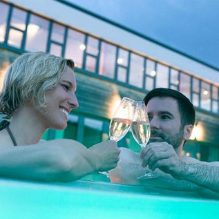 Eltern trinken im Pool des Familienhotels ein Glas Prosecco und geniessen die Aussicht im Outdoor-Pool
