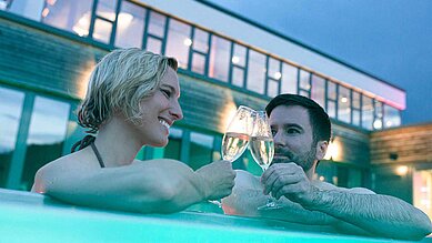 Eltern trinken im Pool des Familienhotels ein Glas Prosecco und geniessen die Aussicht im Outdoor-Pool