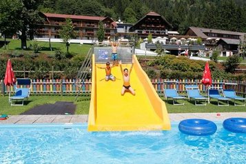 Drei Kinder sausen fröhlich die Wasserrutsche hinunter und landen mit einem Platscher im Pool im Familienhotel Ramsi