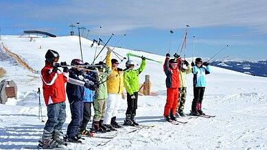 Eine Gruppe fährt Ski und hält die Skistöcke in die Höhe.