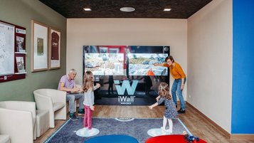 Familie mit zwei Kindern spielt an einer interaktiven iWall-Spielewand im AIGO Welcome Family Bereich.