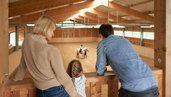 Vater, Mutter und Kind sehen in der Reithalle des Familienhotels Schreinerhof beim Reitunterricht zu.