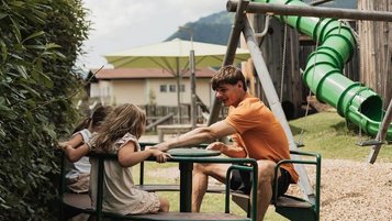 Kinder und ein Betreuer drehen fröhlich ihre Runden auf einem Karussell im Außenbereich des Familienhotels Tirolerhof in Ehrwald