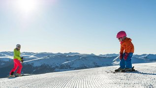 Familie in Kaernten im Winter beim Skifahren. Der Katschberg mit Sonne und blauem Himmel.