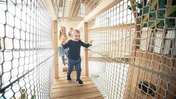 Kinder erkunden lachend den abenteuerlichen Kletterparcours im Indoor Spielbereich des Familienhotels und erleben spannende Momente in luftiger Höhe