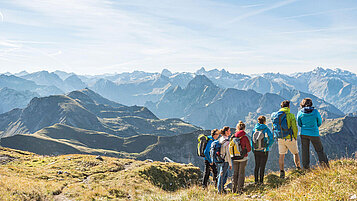 Eine Gruppe von Wanderern genießt die Aussicht vom Nebelhorn im Allgäu. Die Bergketten erstrahlen an diesem Sommertag.