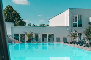 Moderner Außenpool mit Liegebereich und Palmen im Familienhotel Friedrichshof.