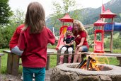 Eine Mutter sitzt mit ihren Kindern am Lagerfeuer und macht Stockbrot mit den Kindern im Familienhotel Bavaria im Allgäu