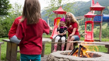 Eine Mutter sitzt mit ihren Kindern am Lagerfeuer und macht Stockbrot mit den Kindern im Familienhotel Bavaria im Allgäu