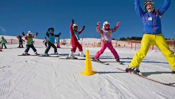 Die Kinder der Kinderskischule fahren ihrer Skilehrerin hinterher und heben dabei ihre Arme in die Höhe. Die Skischule befindet sich ganz in der Nähe des im Familienhotels Feldberger Hof im Hochschwarzwald.