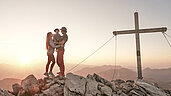 Eltern genießen mit ihrem Kind auf dem Arm den Sonnenaufgang am Gipfel in Liechtenstein