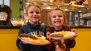 Zwei Kinder halten einen Teller mit Essen hoch und lachen.