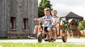Zwei Kinder haben großen Spaß beim gemeinsamen Fahren mit einem Dreirad im Familienhotel.