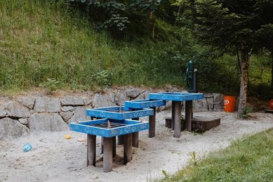 Ein Wasserspielbereich mit blauen Rinnen in einem Sandbereich im Außenareal des Kinderhotels Bruckwirt in Oberösterreich.
