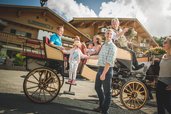 Familienglück auf dem Kutschbock im Landgut Furtherwirt: Ein fröhlicher Kutscher begrüßt lachend eine Familie, während ein kleines Mädchen aus der Kutsche steigt