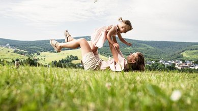 Mutter hebt ihr lachendes Kind in die Luft bei einem Picknick in der Natur nahe eines Familotel.