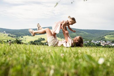Mutter hebt ihr lachendes Kind in die Luft bei einem Picknick in der Natur nahe eines Familotel.