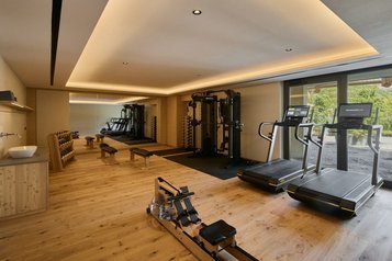Fitnessraum im Familienhotel Bella Vista in Südtirol mit Laufbändern, Trainingsgeräten, Holzboden und Blick ins Grüne.
