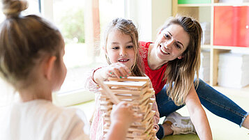 Zwei Mädchen bauen in der Kinderbetreuung des Familienhotels an einem Turm aus Holzklötzen.