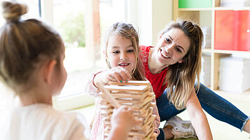 Zwei Mädchen bauen in der Kinderbetreuung des Familienhotels an einem Turm aus Holzklötzen.