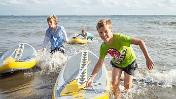 Kinder fahren mit einem SUP am Strand an der Ostsee beim Familienhotel Strandkind
