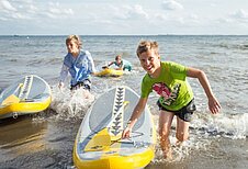 Kinder fahren mit einem SUP am Strand an der Ostsee beim Familienhotel Strandkind