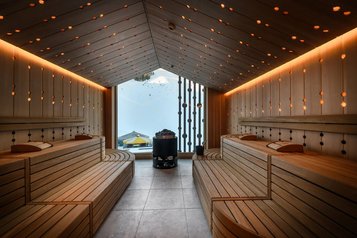 Panoramasauna im Zauchenseehof mit stimmungsvoller Holzverkleidung, warmem Lichtdesign und großem Fenster mit Blick auf die verschneite Berglandschaft.