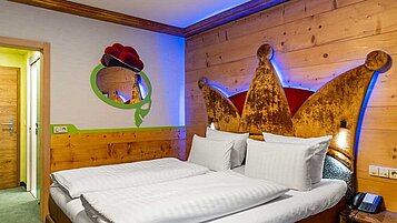 Gemütliches Hotelzimmer im Feldberger Hof mit einem Doppelbett, das ein kunstvolles, kronenförmiges Kopfteil besitzt, und holzvertäfelten Wänden für eine warme Atmosphäre.