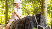 Kleines Mädchen sitzt beim Ausritt in den Wald auf dem Pferd.