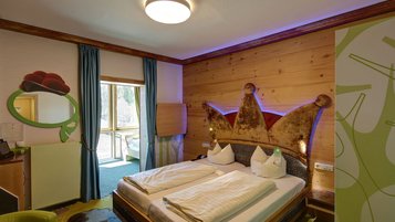 Gemütliches Hotelzimmer im Feldberger Hof mit einem Doppelbett, das ein kunstvolles, kronenförmiges Kopfteil besitzt, und holzvertäfelten Wänden für eine warme Atmosphäre.