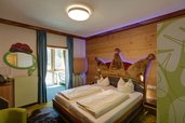 Gemütliches Hotelzimmer im Feldberger Hof mit einem Doppelbett, das ein kunstvolles, kronenförmiges Kopfteil besitzt, und holzvertäfelten Wänden für eine warme Atmosphäre.