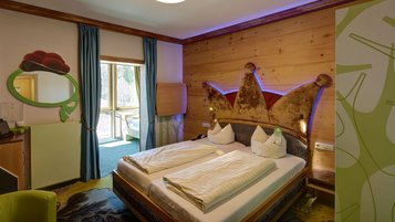 Gemütliches Hotelzimmer im Feldberger Hof mit einem Doppelbett, das ein kunstvolles, kronenförmiges Kopfteil besitzt, und holzvertäfelten Wänden für eine warme Atmosphäre.
