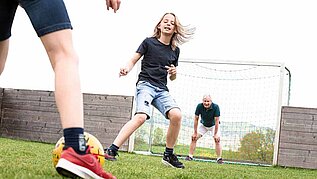 zwei Teenager spielen Fussball mit einem Mann in einem Familienhotel
