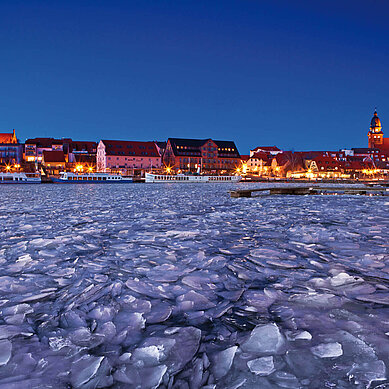 Ein See ist eingefroren mit blick auf eine Stadt im Abendlicht. 