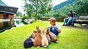 Kleiner Junge sitzt im Freilaufgehege der Hasen und streichelt die Tiere im Familienhotel Alphotel Tyrol Wellness & Family Resort in Südtirol.
